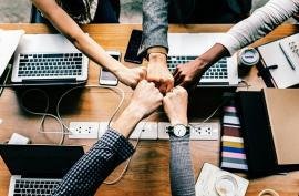 A group of five young adults with technology putting their fists together in a circle