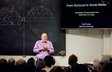 Fred Turner speaks to an audience, showing a slide that says “From Surround to Social Media: Technology and counterculture from World War II to today”